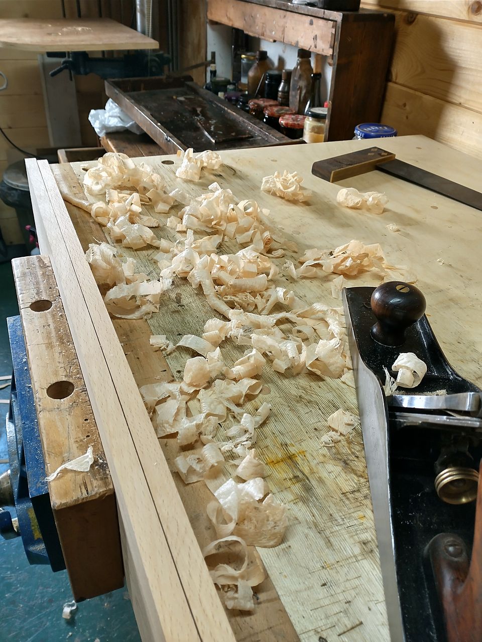 Hand plane and fresh shavings on the workbench beside a board in the vice